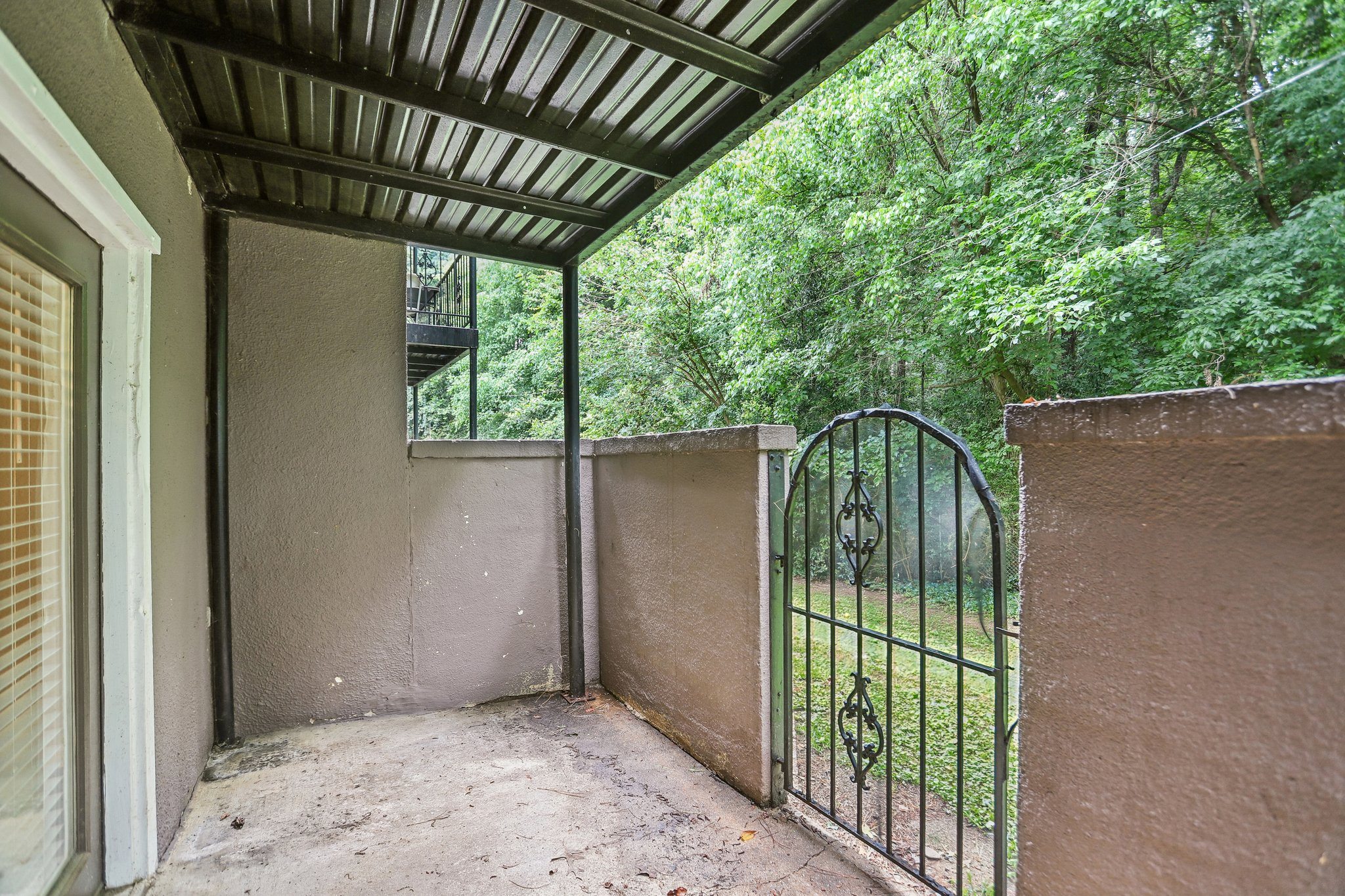 A patio with a metal gate and a view of a green forest.
